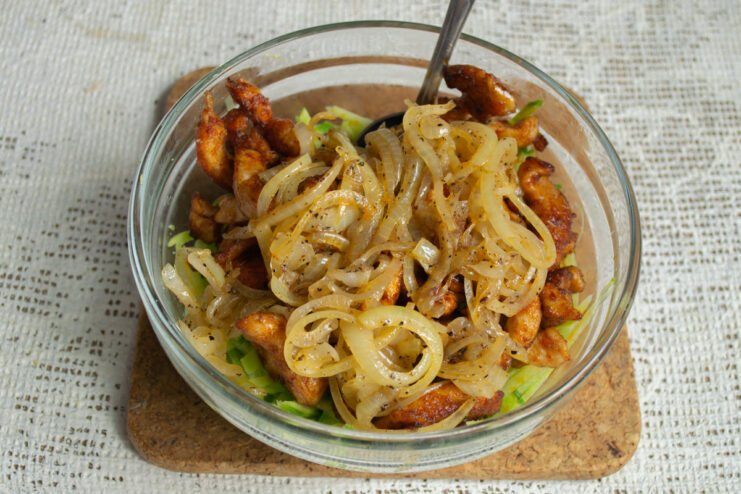 Adding the sautéed onions to the salad. Sautéed onions being added to the bowl with radish and chicken.
