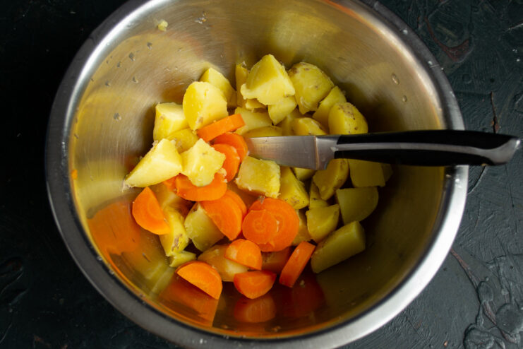 Combining the Salad Vegetables A bowl with diced boiled potatoes and carrots for the salad.