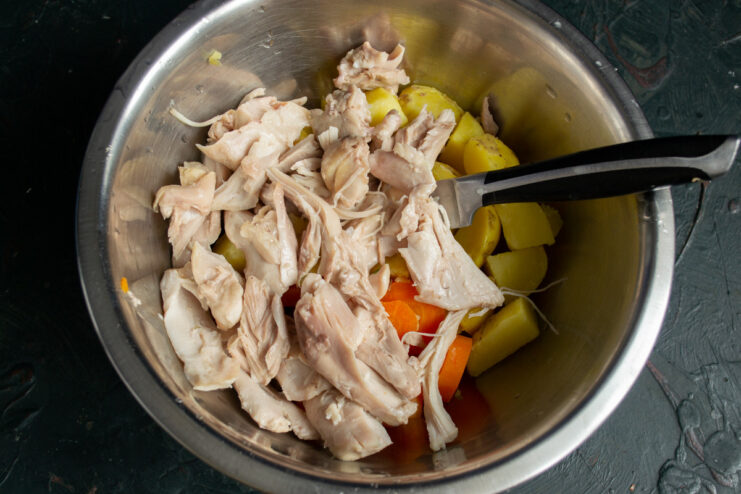 Adding Chicken to the Salad Base Shredded chicken meat being added to a bowl of chopped vegetables.