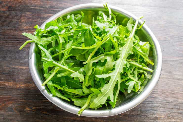 Properly washing and drying arugula is key to a crisp, fresh salad. Fresh arugula leaves being washed in a bowl of water.