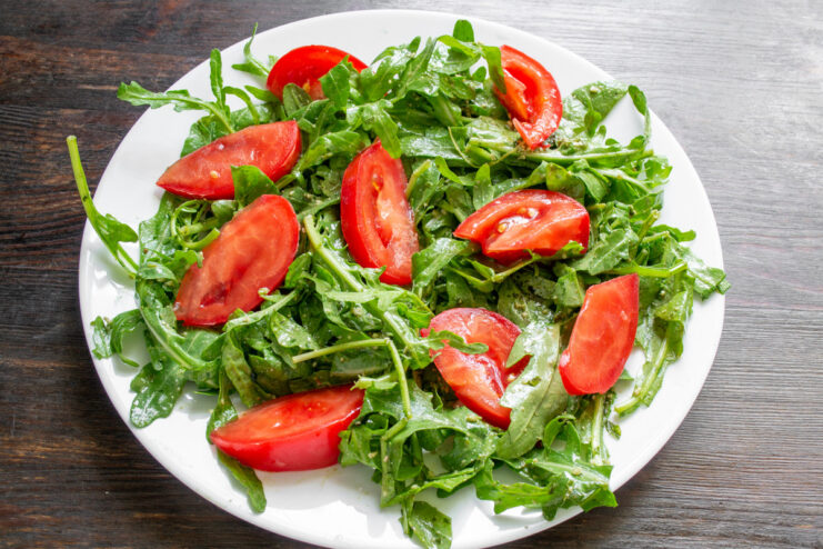 Thick tomato slices add a juicy, substantial bite to the salad. A red tomato being cut into thick slices on a cutting board.
