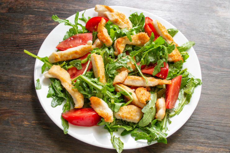The final drizzle of olive oil, balsamic vinegar, and lemon juice brings all the salad flavors together. Assembling the salad: fried chicken pieces are placed on top of arugula and tomatoes before dressing.