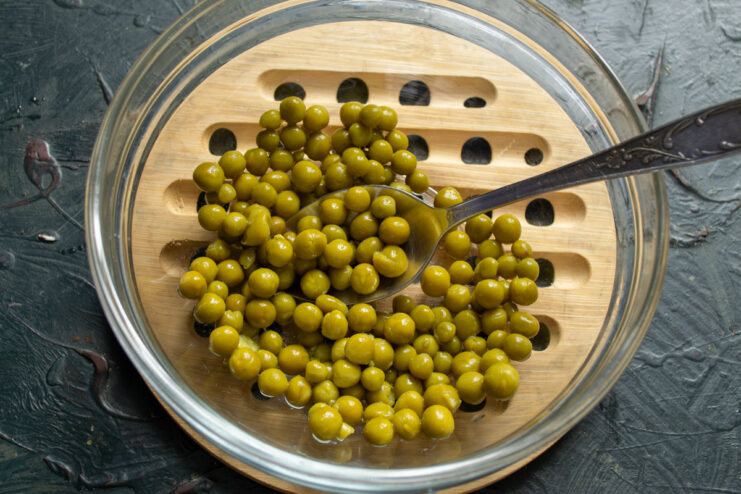 Draining canned green peas for the salad base. A bowl of bright green peas being drained for the salad recipe.