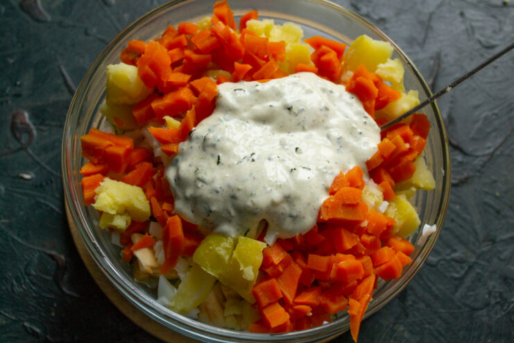 Combining the salad ingredients with the creamy dressing. Adding the prepared dressing to the bowl of chopped salad ingredients and mixing.