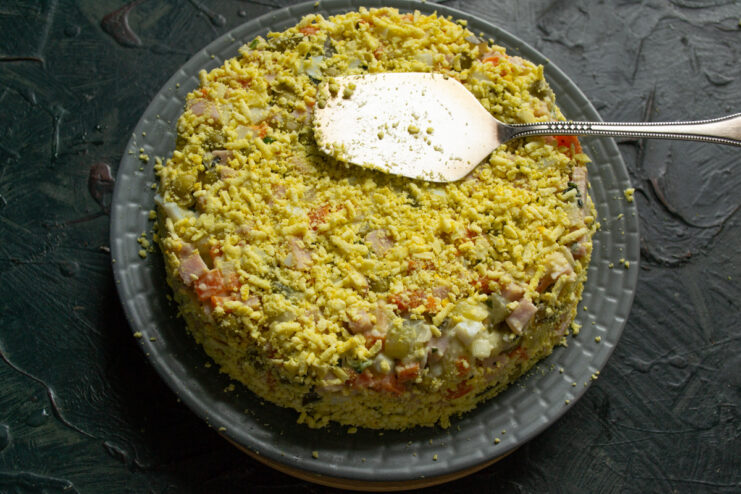 Garnishing the shaped salad with finely grated egg yolk. Sprinkling grated egg yolk over the top and sides of the molded salad.
