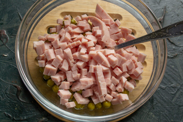 Preparing the chicken ham by dicing it into small, even cubes. Close-up of cooked chicken ham being diced into small cubes on a cutting board.