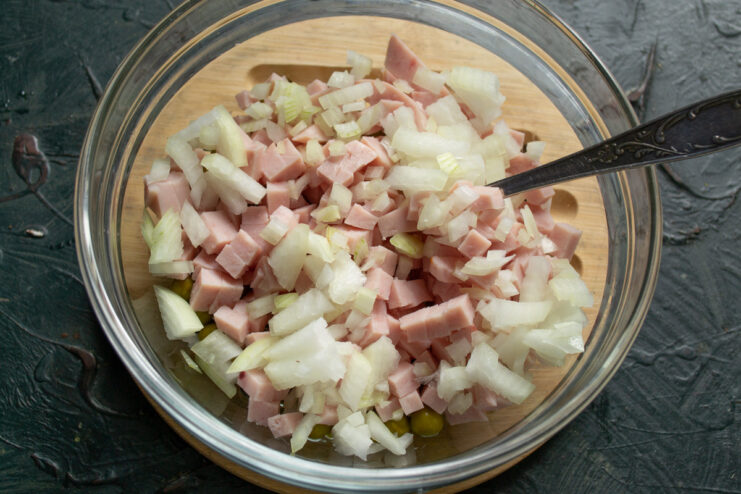 Adding cooled, diced onion to the salad bowl with other ingredients. Diced sweet onion being added to a salad bowl containing green peas and ham.