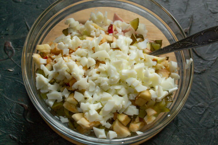 Adding diced hard-boiled egg whites to the salad mixture. Diced hard-boiled egg whites being added to the salad bowl.