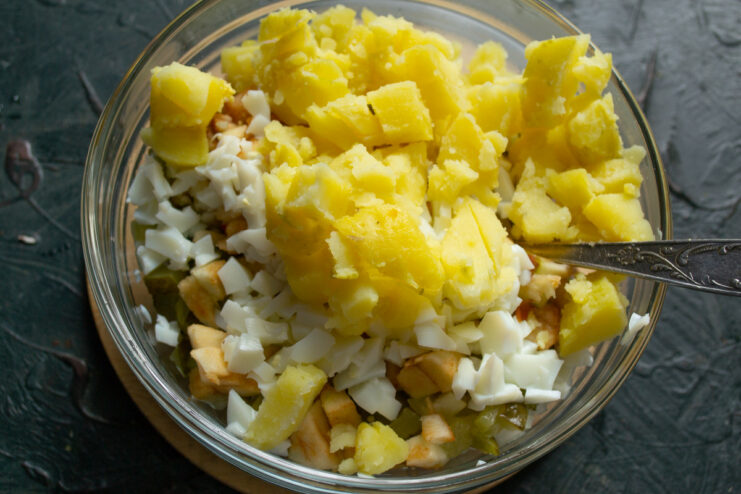 Dicing cooled boiled potatoes for the Stolichny Salad. Cooled boiled potatoes being diced into cubes and added to the salad bowl.