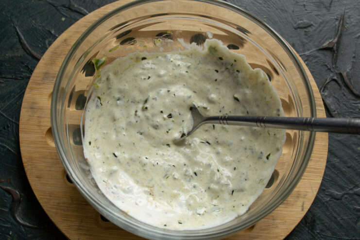 Mixing the salad dressing until smooth and seasoning with salt. The creamy salad dressing being mixed in a bowl with a spoon.