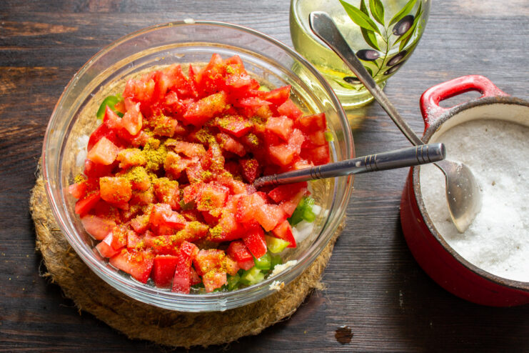 Seasoning the Salsa with Spices and Oil Adding spices and olive oil to the bowl of chopped vegetables for the salsa.