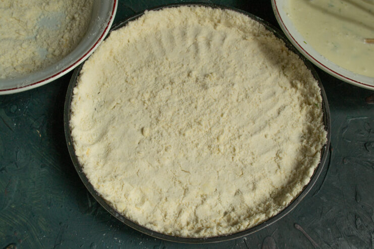 Assembling the Bottom Crust Layer Spreading the first layer of crumble dough evenly in a round baking pan lined with parchment paper.