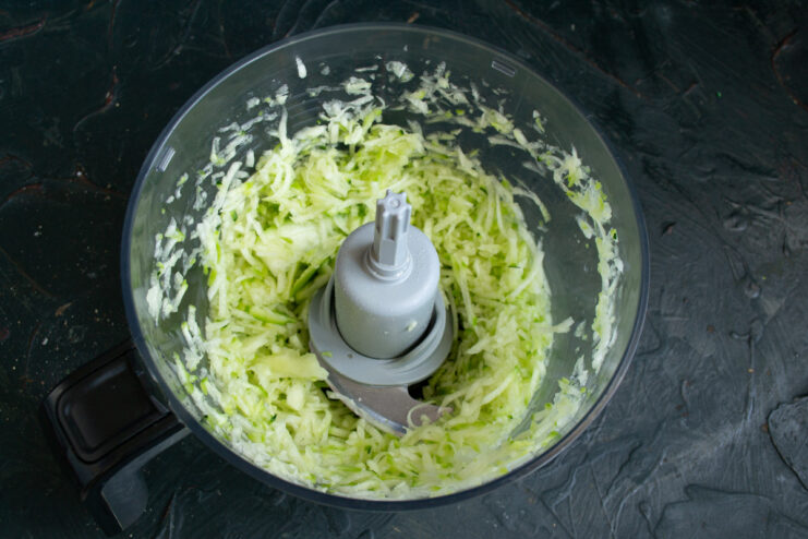 Grate the zucchini coarsely to ensure the pie stays moist and has a great texture. Fresh zucchini being grated on a coarse box grater into a bowl.