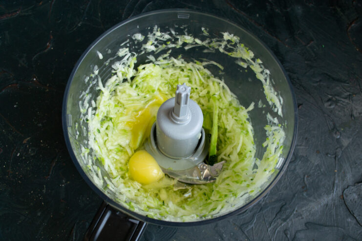 Combine wet ingredients: grated zucchini, eggs, and melted butter for a rich batter. A bowl with grated zucchini, with eggs and melted butter being added.