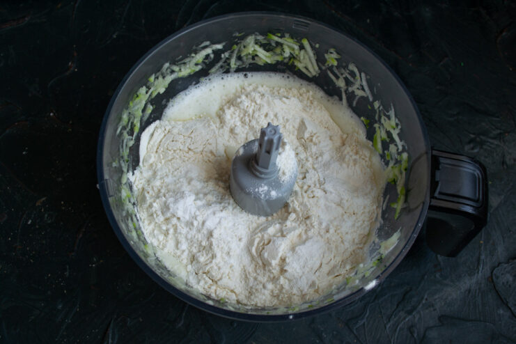 Add the dry ingredients, all-purpose flour and baking powder, to the zucchini mixture. Dry ingredients, flour and baking powder, being added into the wet zucchini mixture.