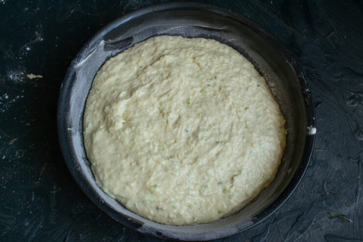 Spread the batter evenly in the prepared baking dish for consistent baking. Zucchini pie batter being spread evenly in a greased and floured baking dish.