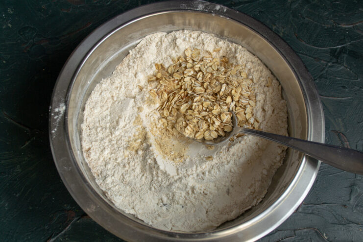 Step 3: Whisking all dry ingredients together for even distribution. Rolled oats being added to the dry ingredients in a bowl.