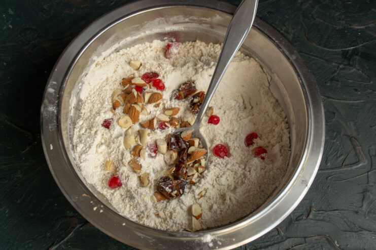 Step 4: Incorporating nuts and dried fruit into the flour mixture. A mix of nuts, dates, and dried cherries being added to the bowl of dry ingredients.
