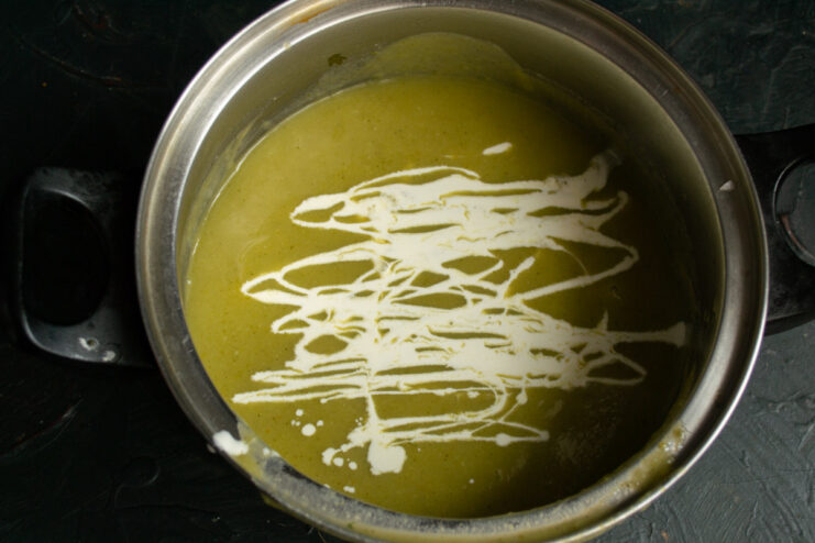 Finishing the Soup with Cream and Seasoning Pouring cream into the strained vegetable soup in a pot.