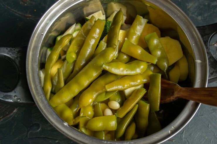 Adding Parboiled Green Beans to the Soup Parboiled green beans being added to the pot of vegetables.