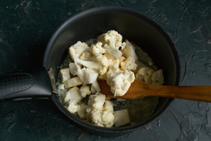 Breaking down the cauliflower into small florets. A head of cauliflower being broken into small florets.