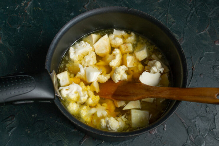 Adding liquid to the vegetables in the pot. Pouring boiling water or broth over the vegetables in a pot.