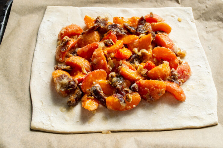 Evenly spreading the apricot and date filling over the puff pastry base. The apricot and date filling spread evenly over a sheet of puff pastry.