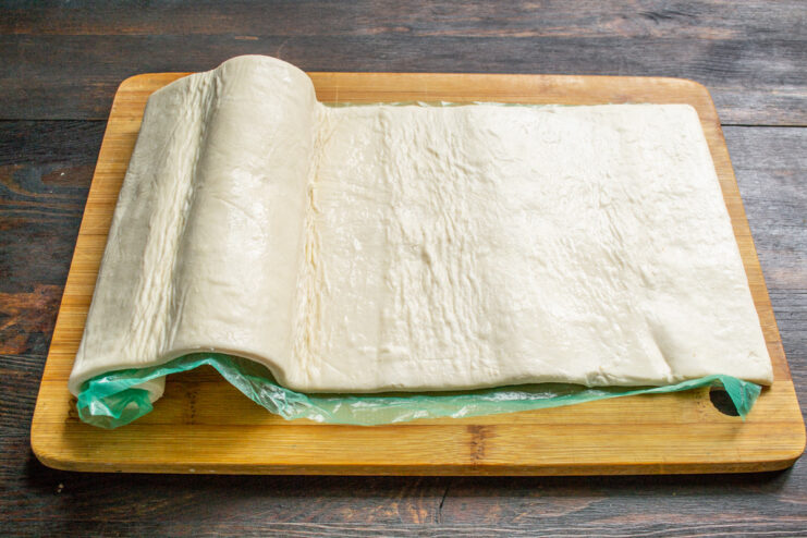Preparing the puff pastry: Thaw the frozen sheet before rolling. A sheet of frozen puff pastry being unfolded on a work surface.