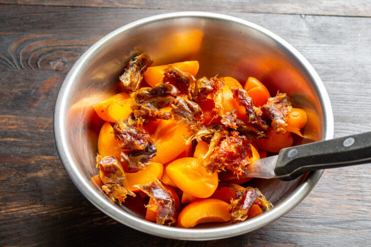 Adding chopped dates to the apricot filling for extra sweetness. Chopped dates being added to a bowl of sliced apricots.