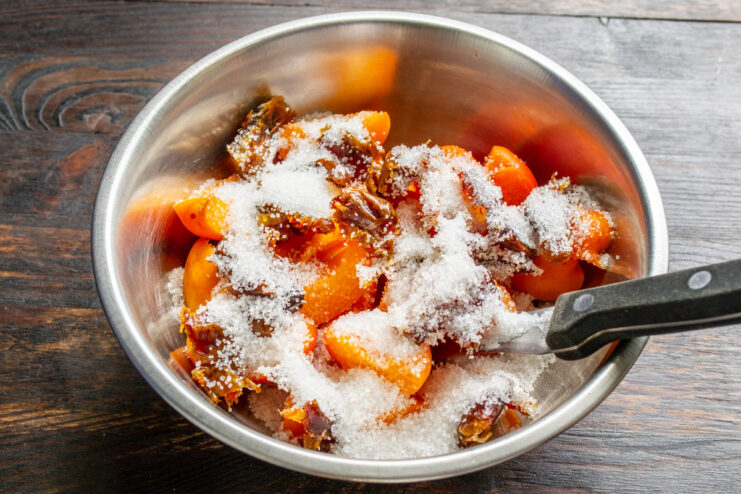 Sprinkling sugar into the fruit filling to sweeten the pie. Adding granulated sugar to the bowl with apricots and dates.