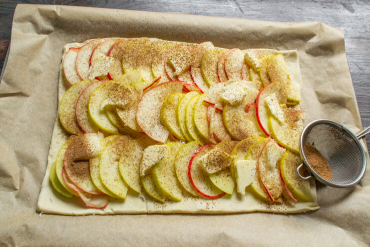 Sprinkling ground cinnamon over the apple filling using a small sieve.