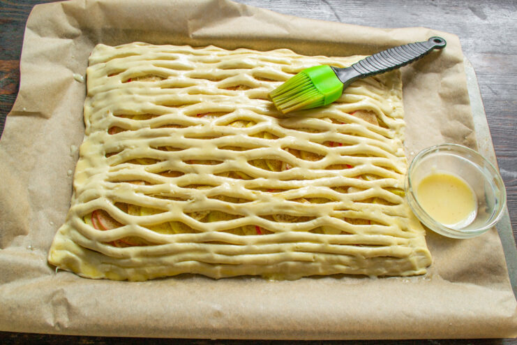 Brushing the top of the puff pastry pie with an egg wash before baking.