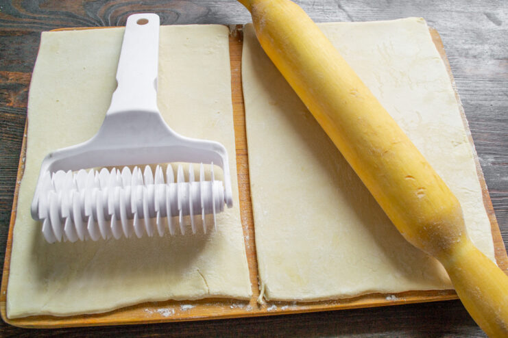 A sheet of rolled-out puff pastry being cut in half with a knife.