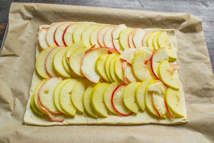 Placing the assembled pie base with apples onto a parchment-lined baking sheet.
