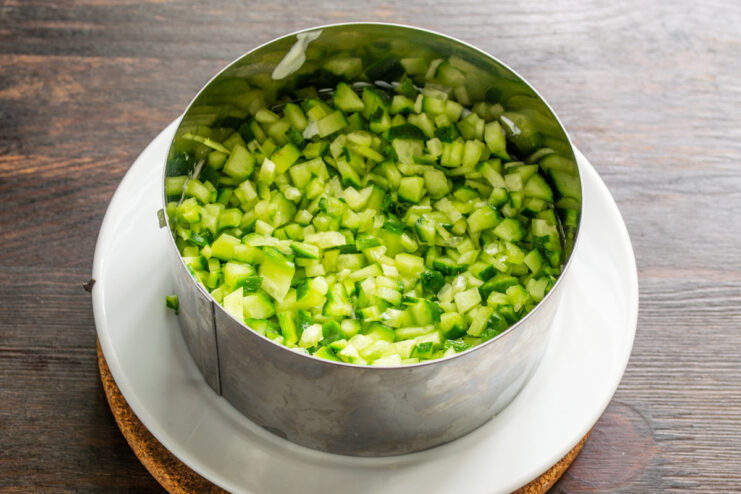 Dicing Fresh Cucumbers for a Crunchy Layer Fresh cucumbers being finely diced on a cutting board.
