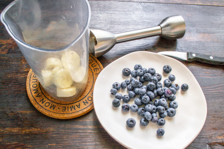 Step 2: Adding Fresh Blueberries for Flavor and Color A handful of fresh blueberries being added to the blender cup with the banana.