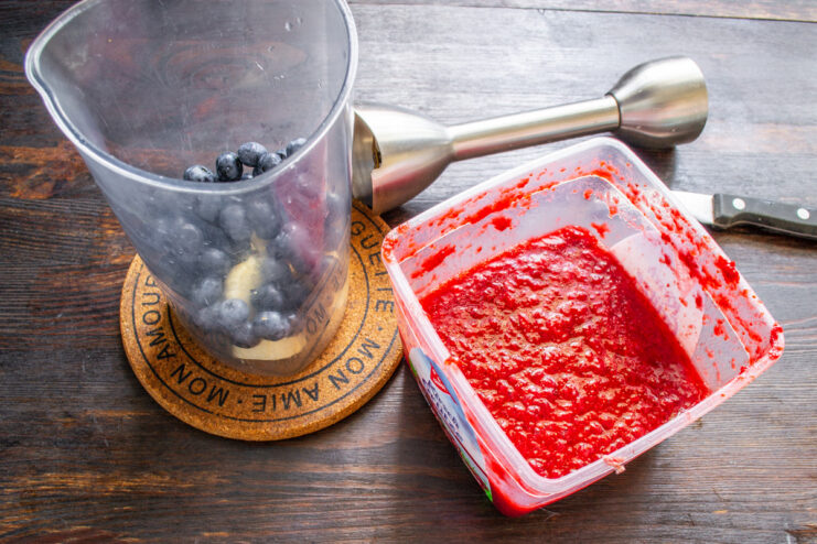Step 3: Incorporating Strawberry Puree for Sweetness Strawberry puree being added to the blender cup on top of bananas and blueberries.