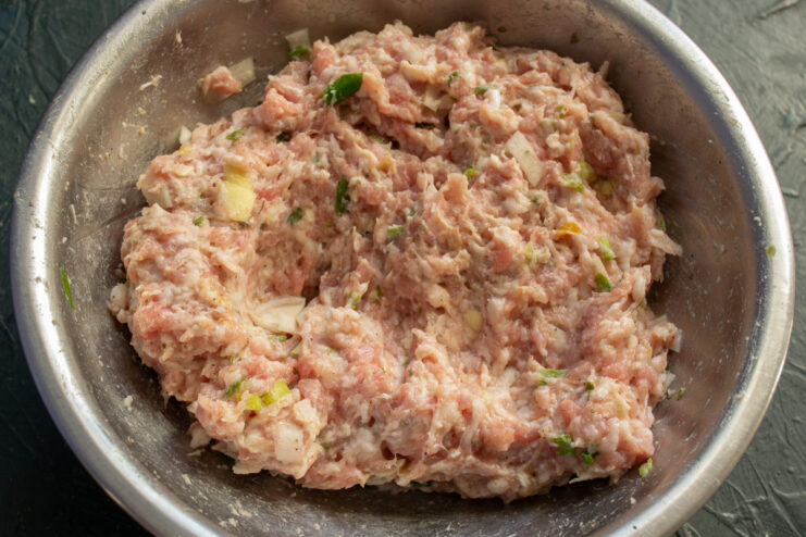Thoroughly mixing the cutlet mixture by hand. Hands in gloves mixing the ground meat, onions, and milk in a bowl.