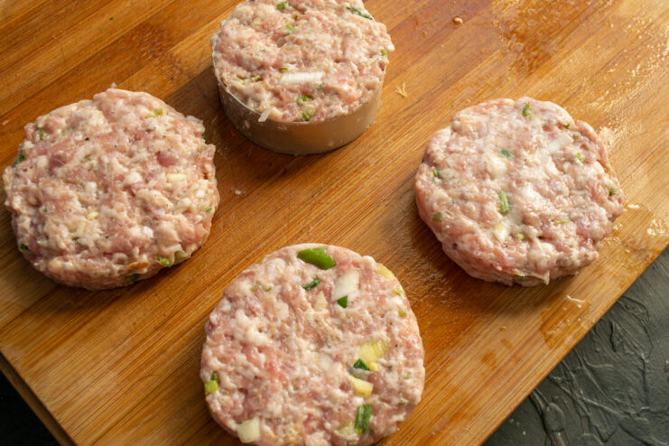 Forming the ground meat mixture into thick, round patties. Four perfectly formed raw meat patties ready for cooking.