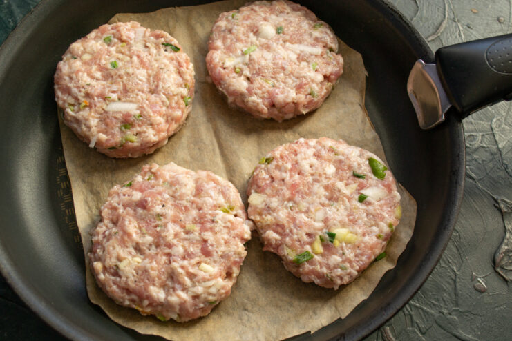 Placing the cutlets on parchment paper in a hot pan. Raw meat patties placed on a sheet of parchment paper in a frying pan.