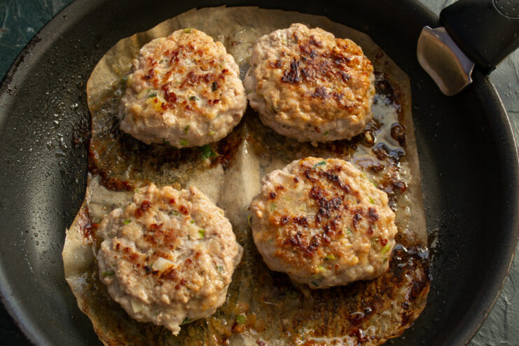 Flipping the cutlets to cook the other side. Cutlets being flipped in the pan while cooking on parchment paper.