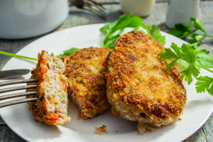 A plate with a golden-brown pork schnitzel with bell pepper, garnished with fresh herbs.