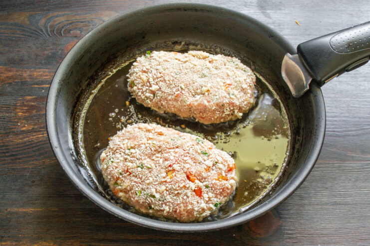 Frying the Pork Schnitzels to a Golden Brown Two pork schnitzels being placed into a hot skillet with oil.