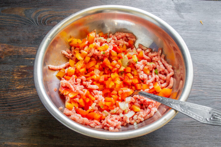 Combining Ingredients for Pork Schnitzel Patties A bowl of ground pork mixed with diced onion and red bell pepper.