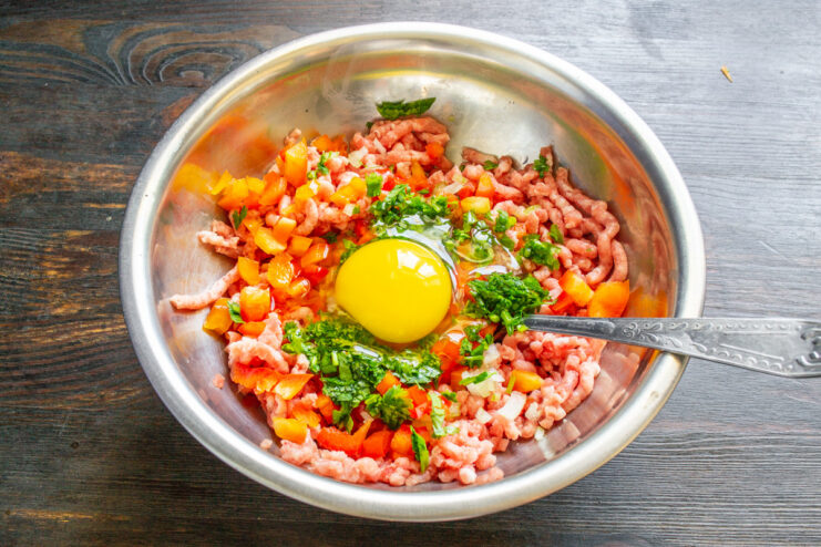 Binding the Schnitzel Mixture with an Egg A large egg cracked into a bowl with the pork and vegetable mixture.