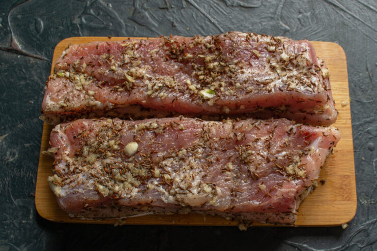 Spice Rub Variation 1: Garlic and Caraway A piece of cured pork belly being generously coated with a garlic and caraway seed spice rub.