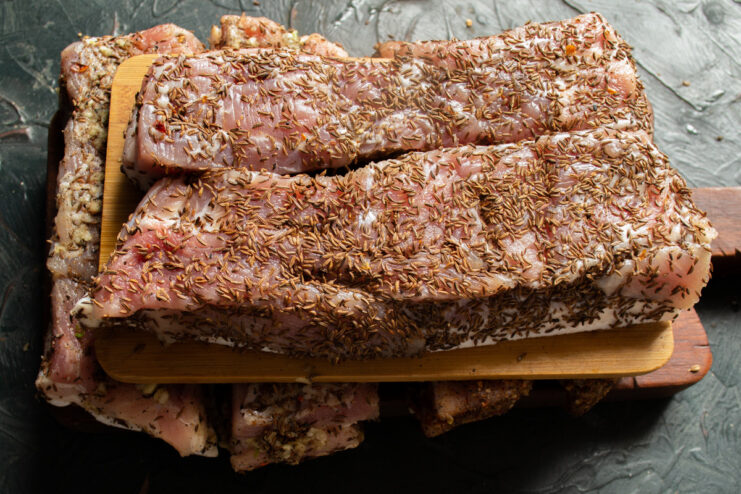 Final Step: Chilling the Seasoned Pork Belly Three pieces of cured pork belly, each with a different spice rub, resting on a wooden board.