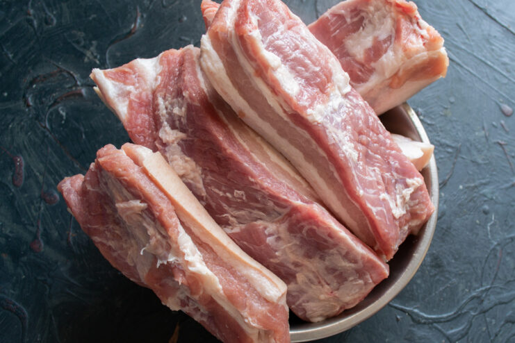 Step 2: Measuring Salt for the Pork Brine A bowl of coarse salt next to pieces of raw pork belly, ready for making the brine.