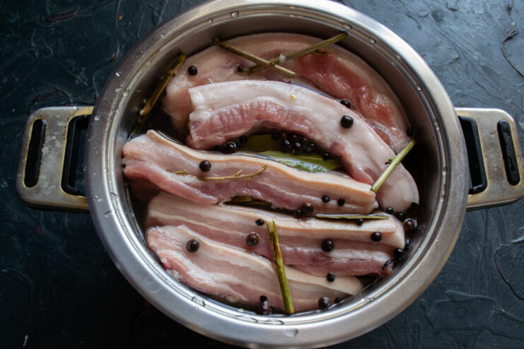 Step 5: Submerging the Pork Belly in Brine Strips of pork belly being placed into a large container filled with brine.