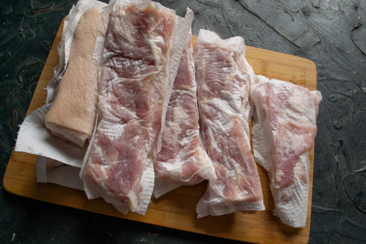 Step 8: Drying the Cured Pork Belly Cured pork belly pieces being patted dry with paper towels on a cutting board.